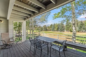 Une terrasse extérieure couverte, dotée d’une table et de chaises, qui donne sur un espace verdoyant avec des arbres.