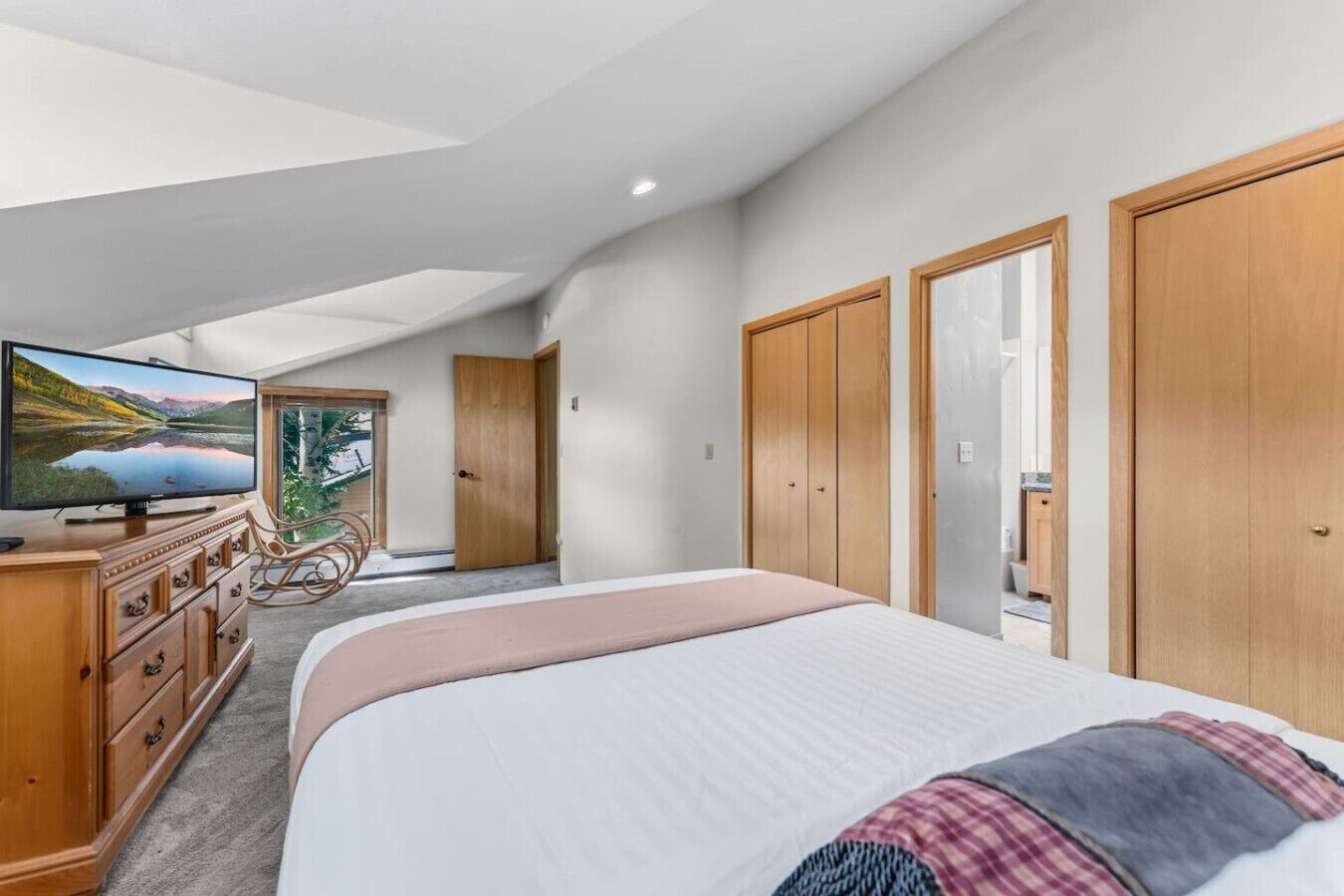 Un dormitorio moderno con una cama grande, un armario de madera y un televisor sobre un aparador de madera.