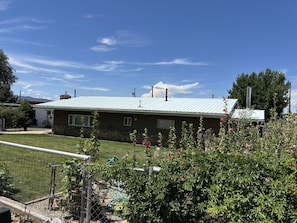 A residential house with a metal roof, stone foundation, and a fenced yard with flowering plants.