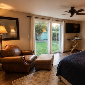 A bedroom with a bed, a leather armchair, an ottoman, a TV, and a ceiling fan.