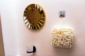A wall with a round mirror, a wall-mounted hook, and a wall-mounted cup holder.