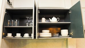 Armário de cozinha com prateleiras contendo copos, chávenas e um bule.