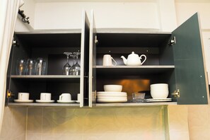 A kitchen cabinet with shelves containing glassware, cups, and a teapot. - Luxury Studio Apartment in Kimana Near Amboseli (Oloitokitok)