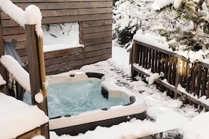 Ein Whirlpool in verschneiter Winterlandschaft mit einer Holzterrasse und einem Holzzaun.