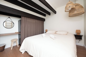 A bedroom with a large bed, a hanging light fixture, a bedside table with a lamp, and a small stool. - 5 passengers • Air Conditioning • Free parking • Downtown on foot (Albi)