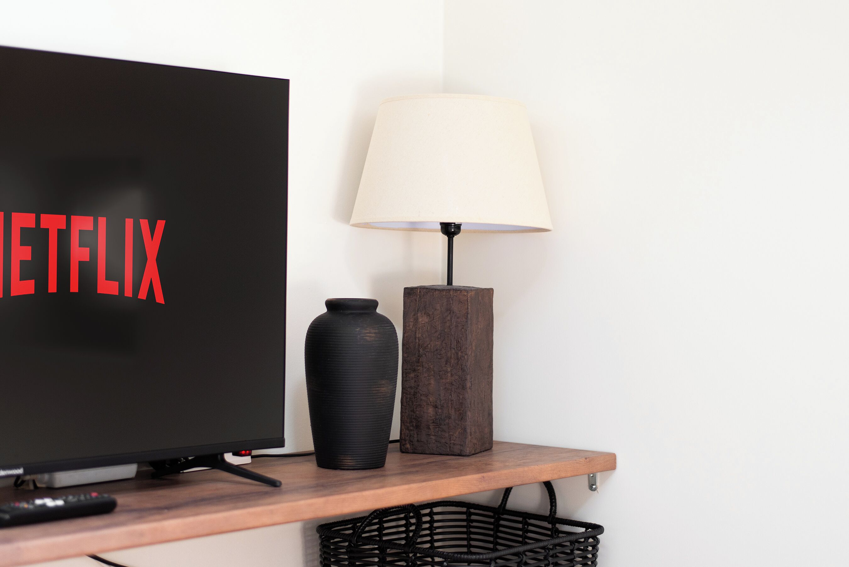 A television with the Netflix logo, a lamp, and a remote control on a wooden shelf.