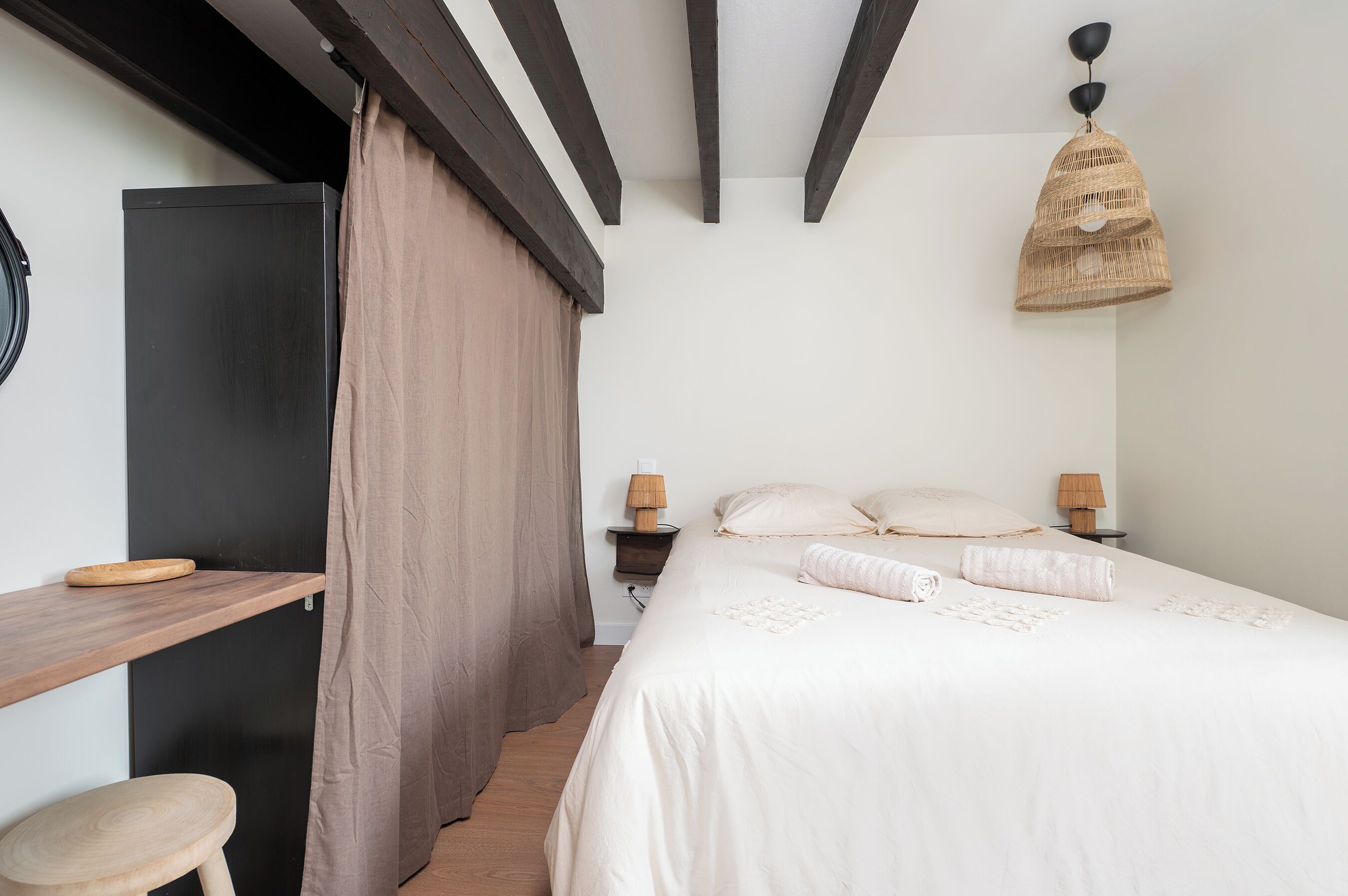 A bedroom with a bed, bedside lamps, a wooden desk, a chair, and a hanging light fixture.