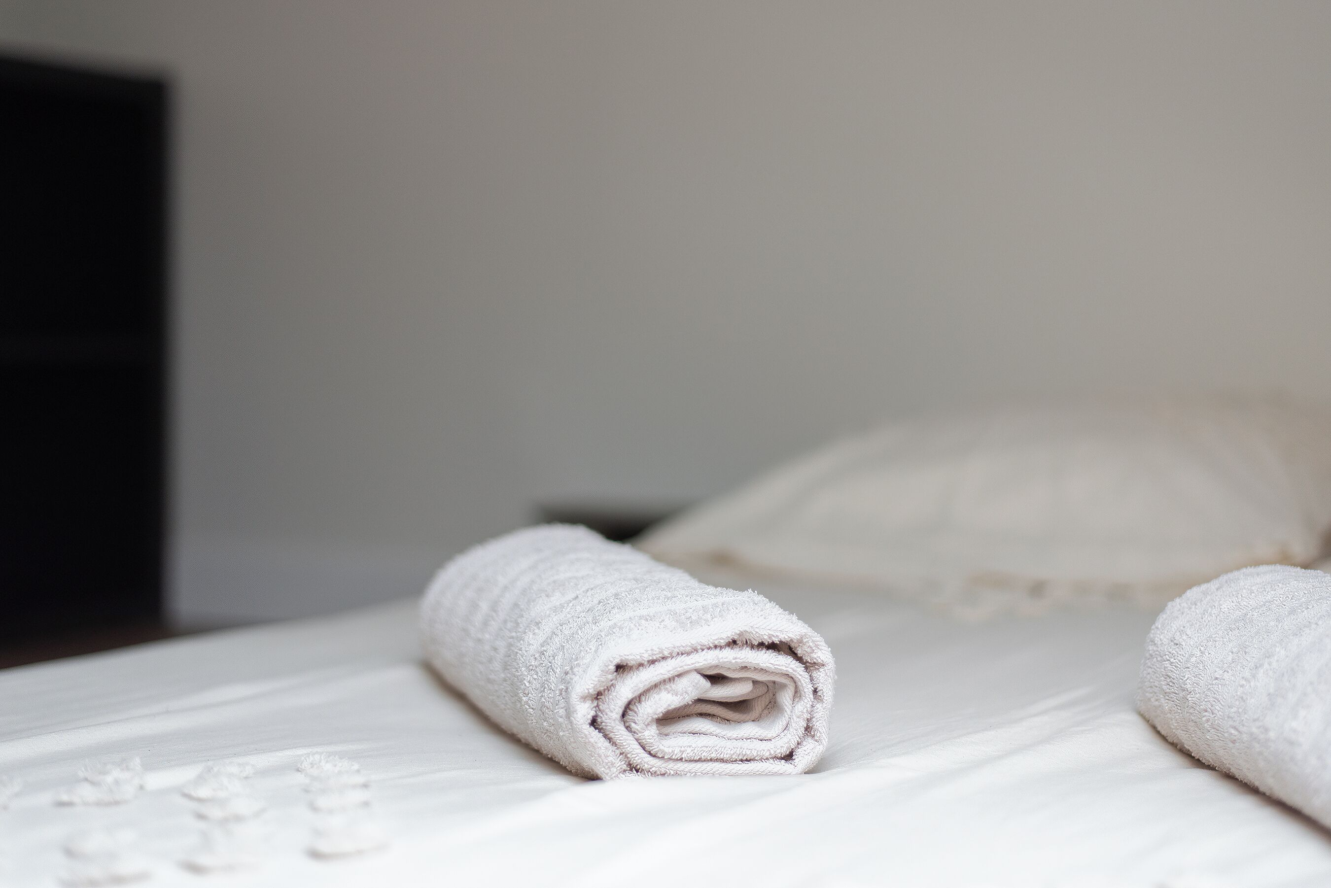A neatly made bed with a rolled white towel on it.