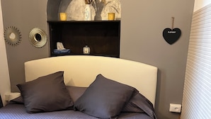 A neatly made bed with rolled towels, a headboard, and a decorative mirror on the wall.