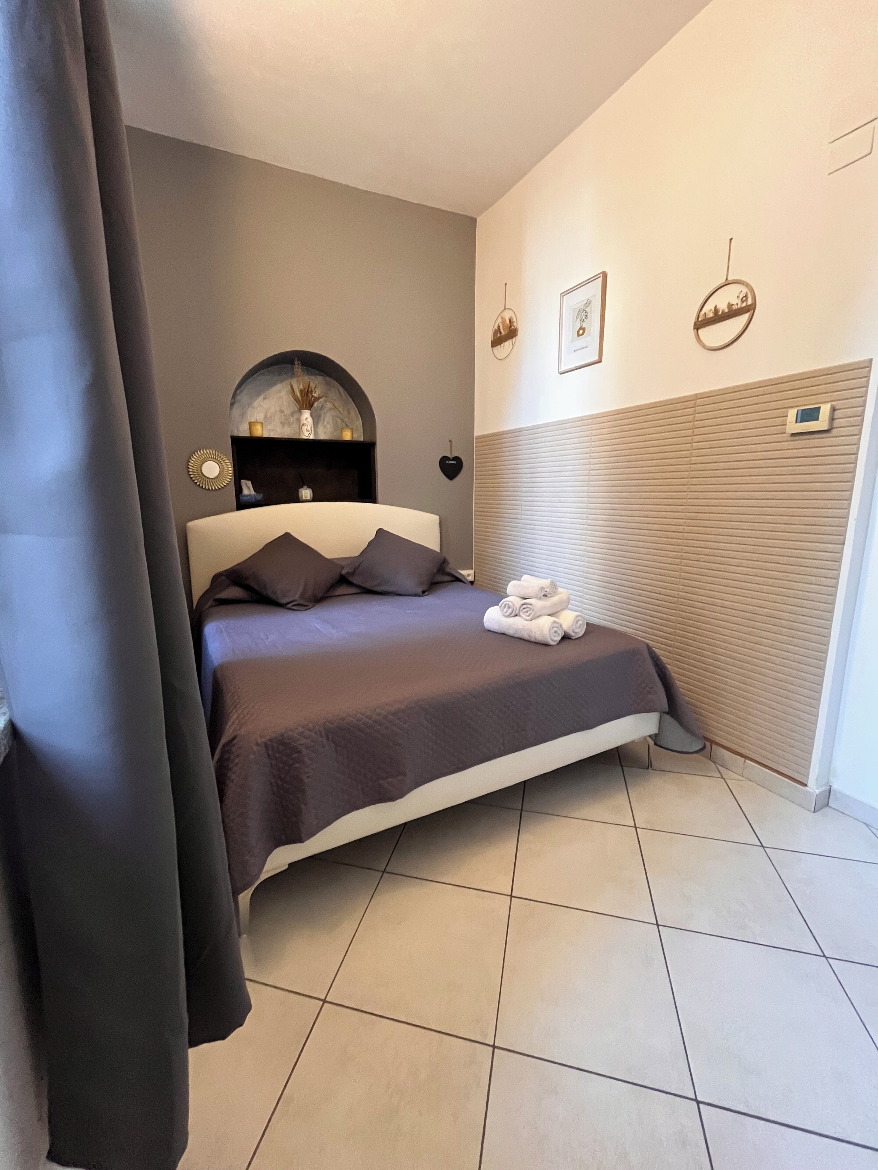 Una camera da letto con un letto, una testiera, un comodino, una mensola a muro e una finestra con persiane.