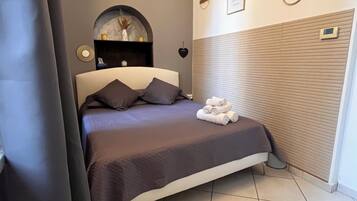 Una camera da letto con un letto, una testiera, un comodino, una mensola a muro e una finestra con persiane.