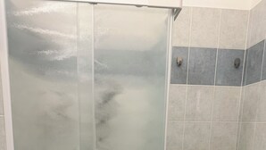A glass-enclosed shower stall with a white towel rack and a shelf holding towels and toiletries.