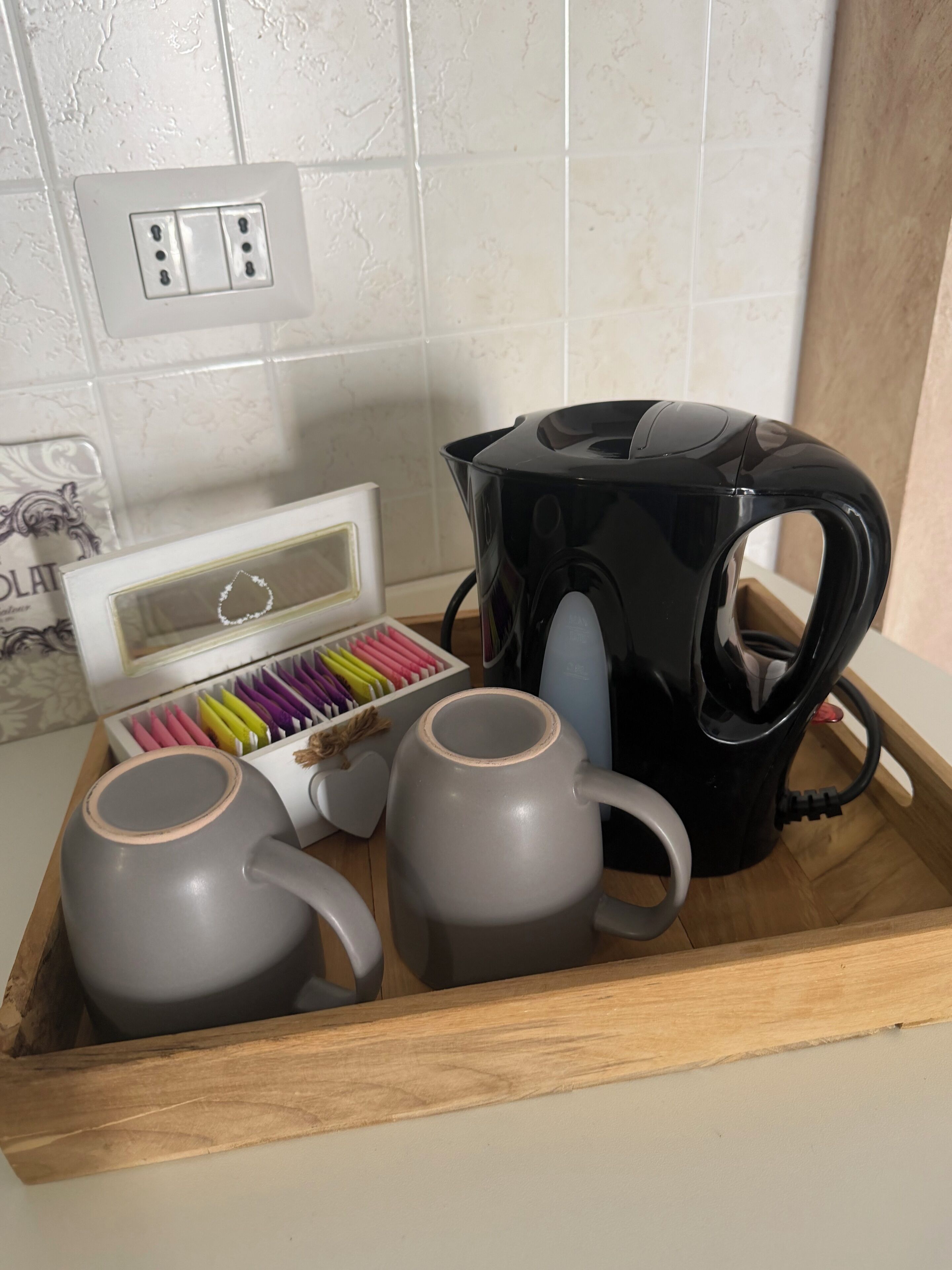 A wooden tray with two grey mugs and a black electric kettle.