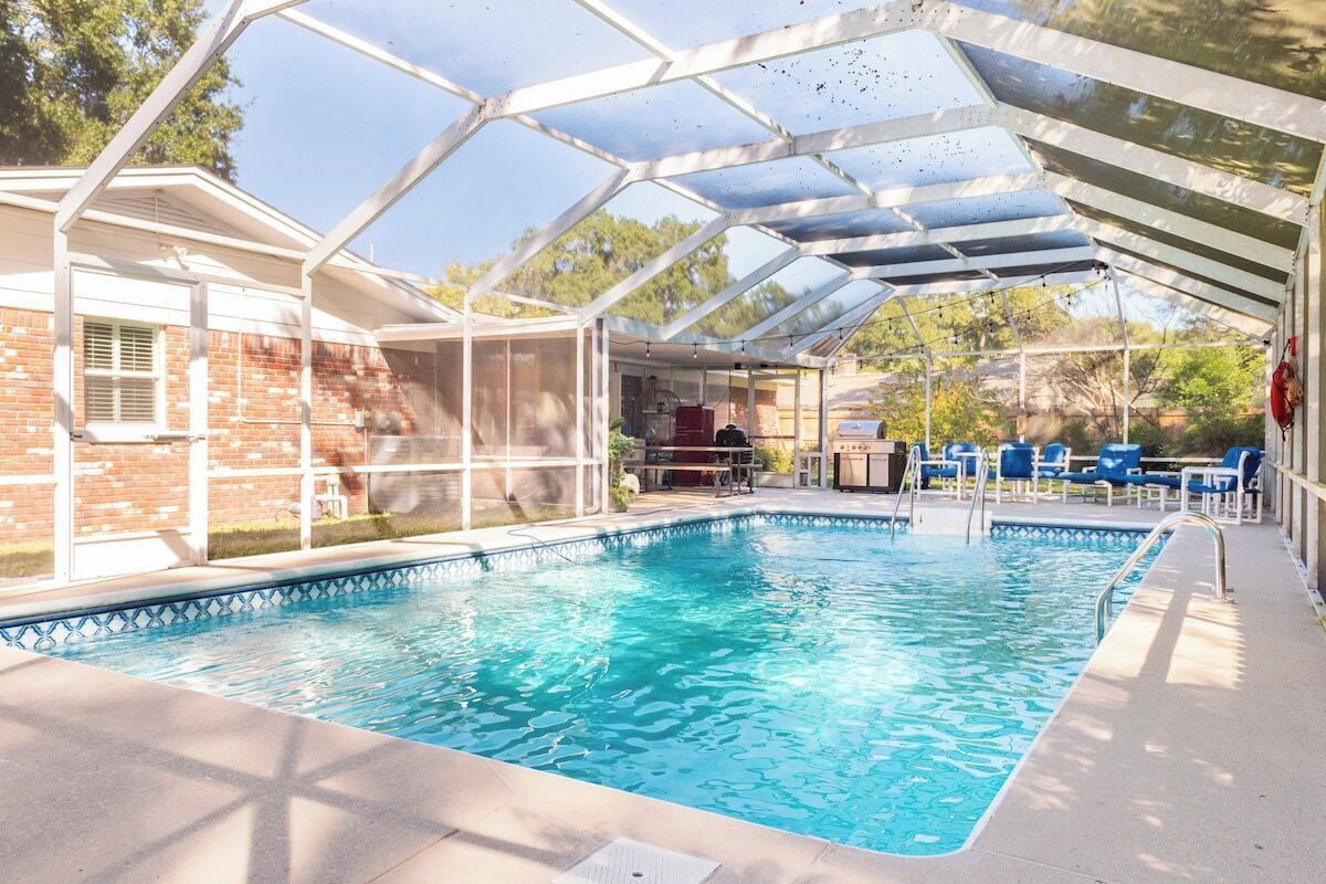A covered swimming pool with a glass roof, surrounded by lounge chairs and a barbecue area.