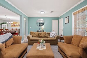 A living room with a sofa set, a coffee table with a vase, and a dining area with a painting.