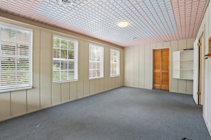 A room with a sloped ceiling, large windows with blinds, a wooden door, and a carpeted floor. - Local on Lamar. 5 min to square or campus. Ranch-style home on S Lamar. (Oxford)