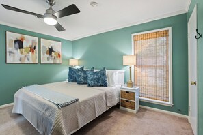 A bedroom with a bed, two wall-mounted lamps, a ceiling fan, and two abstract paintings.
