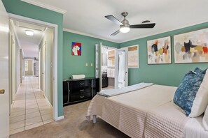 A bedroom with a bed, a ceiling fan, a dresser, and artwork on the walls.