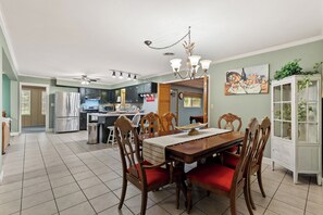 A spacious kitchen with modern appliances, a dining area with wooden chairs and a red cushion, and a white cabinet with glass doors.