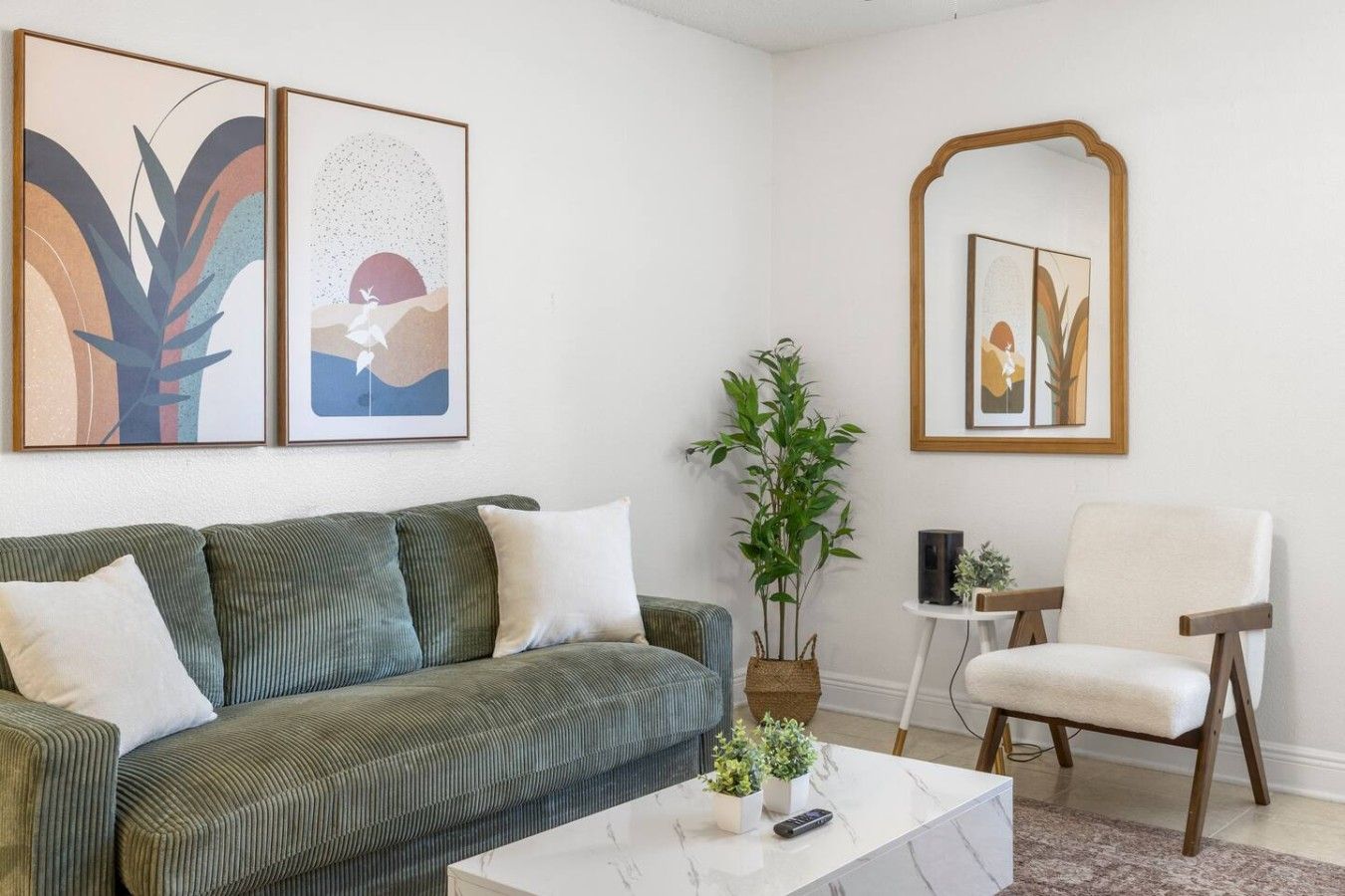 Een woonkamer met een groene bank, een witte salontafel, een spiegel en twee kunstwerken in lijsten aan de muur.