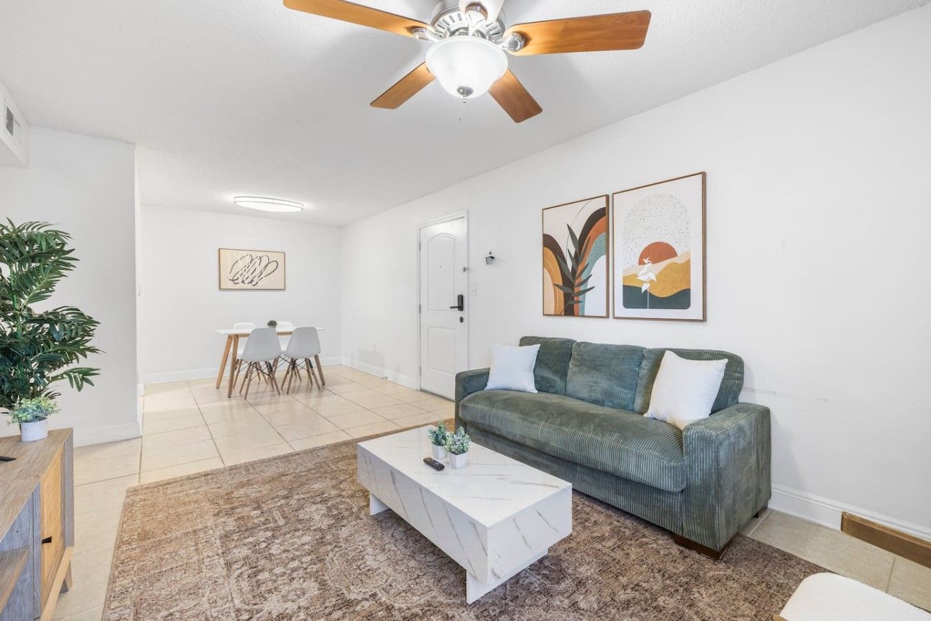 Een woonkamer met een plafondventilator, een bank, een salontafel en een eethoek met stoelen en een tafel.