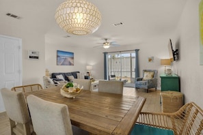 A dining area with a wooden table and chairs, a ceiling fan, and a large window with curtains. - Miramar Beach Getaway Steps away from the beach (Miramar Beach)