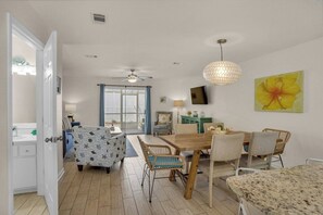 Un coin repas avec une table et des chaises en bois, un ventilateur de plafond et un téléviseur fixé au mur.