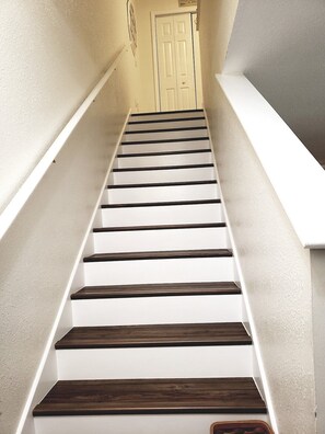 Un escalier avec des marches blanches et des contremarches en bois foncé menant à une porte.