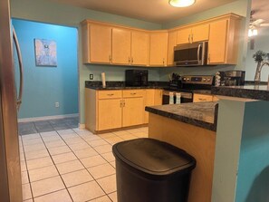 A kitchen with wooden cabinets, a microwave, a coffee maker, and a trash bin.