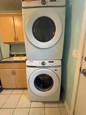 A stacked washer and dryer unit in a kitchen with wooden cabinets and a tiled floor.
