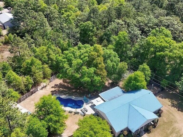 An aerial view of a property with a swimming pool, a covered patio, and a large house with a blue roof.