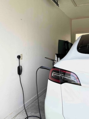 A white car parked indoors with a charging cable connected to a wall socket. - Miramar Beach Townhouse: Pool, Steps from the beach (Miramar Beach)