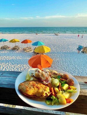 A beach scene with a plate of food in the foreground and beach umbrellas in the background. - Miramar Beach Townhouse: Pool, Steps from the beach (Miramar Beach)