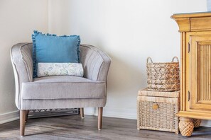 Un fauteuil à revêtement gris avec un coussin bleu, un panier en osier et un meuble en bois.