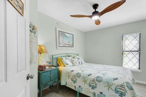 A bedroom with a bed, a nightstand, a ceiling fan, a window with blinds, and a wall-mounted picture. - Gorgeous Waterfront Home! (Fort Walton Beach)