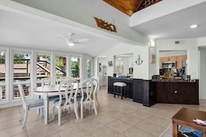 A spacious kitchen with a dark countertop and white cabinetry, a dining area with white chairs and a table, and a large window offering a view of the outdoors. - Gorgeous Waterfront Home! (Fort Walton Beach)