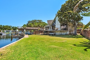A waterfront property with a grassy lawn, a dock with boats, and a large tree. - Gorgeous Waterfront Home! (Fort Walton Beach)