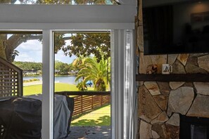 Una habitación con chimenea de piedra, televisor montado en la pared y vistas a un lago y vegetación.
