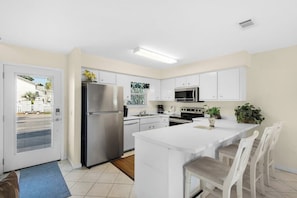 A modern kitchen with white cabinetry, stainless steel appliances, and a central island with seating. - Beachfront Townhome w/ Pool (Destin)