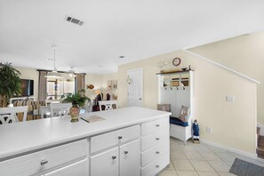 A kitchen with a white countertop, a dining area with chairs, a staircase, and a clock on the wall. - Beachfront Townhome w/ Pool (Destin)