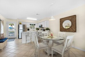 A modern kitchen with white cabinets, a refrigerator, and a dining area with a glass table and white chairs. - Beachfront Townhome w/ Pool (Destin)
