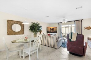 A living room with a sofa, a dining table with chairs, a television, and a ceiling fan. - Beachfront Townhome w/ Pool (Destin)