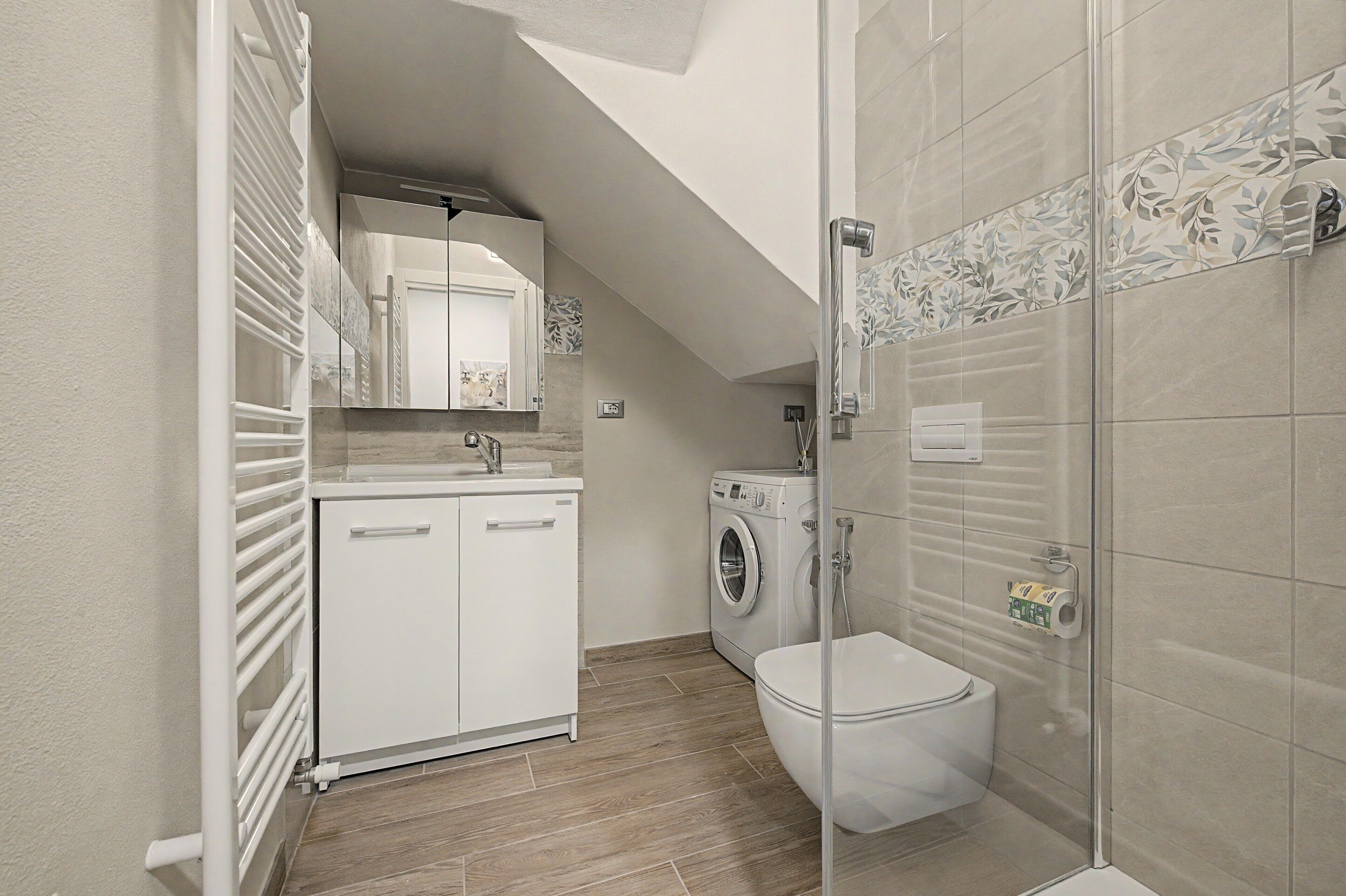 A compact bathroom with a shower, toilet, and a washing machine.