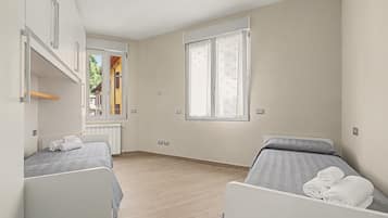 A hotel room with two beds, a window with curtains, a radiator, and a view of a building outside.