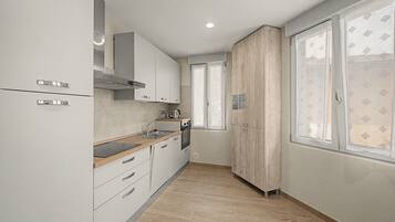 Eine moderne Küche mit weißen Schränken, einer Holz Arbeitsplatte und einem Fenster mit gemusterten Vorhängen.