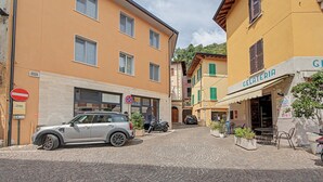 A cobblestone street with buildings on either side, a parked car, and a gelateria with outdoor seating.