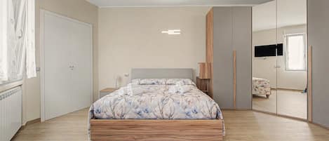 Un dormitorio con cama, armario, espejo y televisor.