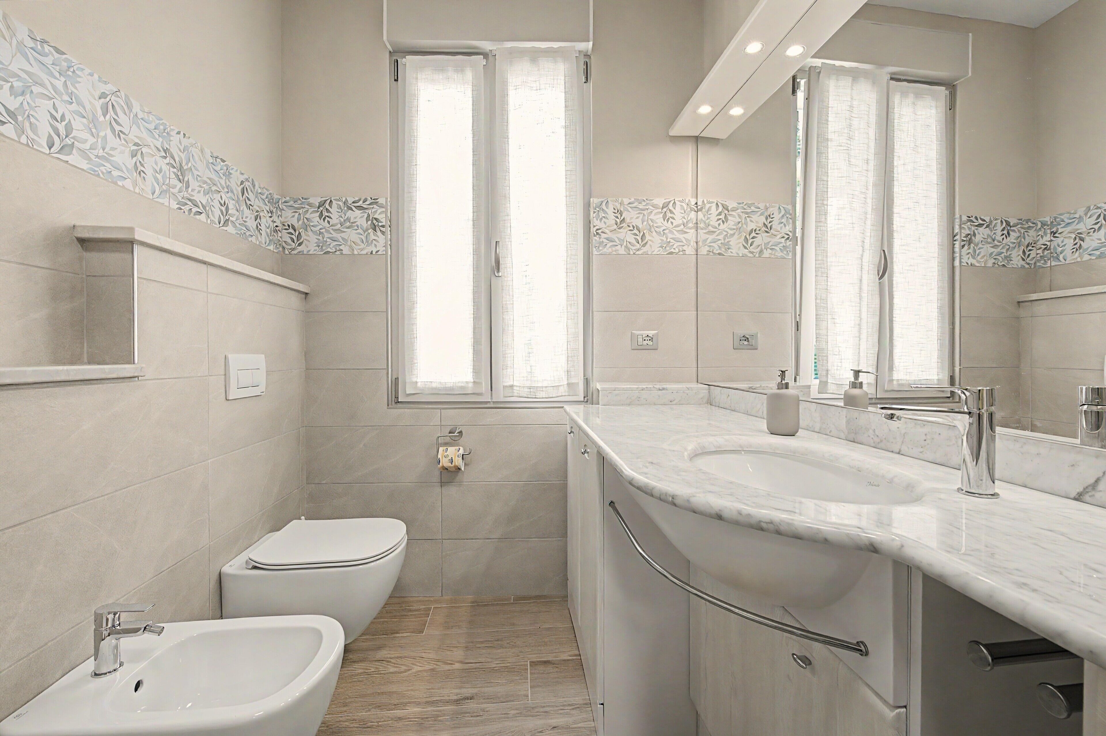 Een moderne badkamer met een toilet, een wastafel, een spiegel en een bidet.