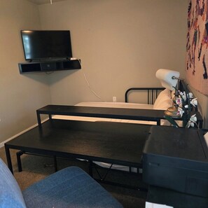 A small, simple room with a bed, a television mounted on the wall, a desk, and a lamp with flowers. - Pet-Friendly Townhome w/ Fire Pit, 5mins to Beach (Fort Walton Beach)