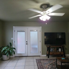 A living room with a ceiling fan, a television on a wooden stand, a door with frosted glass panels, and a potted plant. - Pet-Friendly Townhome w/ Fire Pit, 5mins to Beach (Fort Walton Beach)